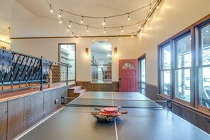 Une table de ping-pong dans une pièce dotée de grandes fenêtres, d’un miroir et d’un escalier.