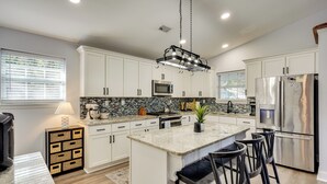 A modern kitchen with white cabinets, a central island with bar stools, a stainless steel refrigerator, and a microwave. - Coastal Convenience! Mt Pleasant Gem 2 Mi to Ocean (Mount Pleasant)