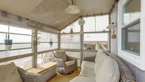 Una habitación iluminada por el sol, con muebles de mimbre, una mesa de madera y vistas al mar a través de amplias ventanas.