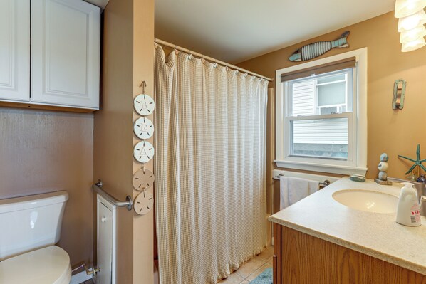 A bathroom with a toilet, a shower curtain, a sink, and a window. - Walk to Public Beach: Bayfront Jersey Home w/ View (Newport)