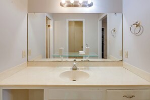 Une salle de bain avec un lavabo blanc, une commode avec un plateau en verre, un miroir et un porte-serviettes.