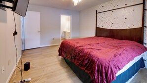 A bedroom with a bed, a ceiling fan, a TV mounted on the wall, and a power strip on the floor.