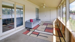 A covered porch with a gray sofa, a red pillow, and a patterned rug.