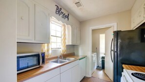 A kitchen with white cabinets, a black refrigerator, a microwave, and a window with curtains.