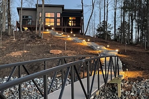 Une maison moderne dotĂ©e dâune terrasse en bois, dâun escalier en pierre et dâune rambarde en mĂ©tal.
