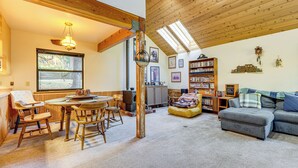 A cozy living room with a fireplace, wooden furniture, a bookshelf, and a large window. - 1 Mi to Skiing! Cabin Hideaway on June Lake Loop (June Lake)