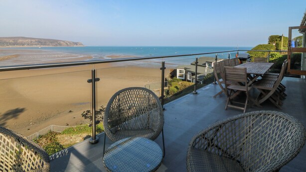Un balcon meublé avec des meubles en osier, donnant sur une plage et l’océan.