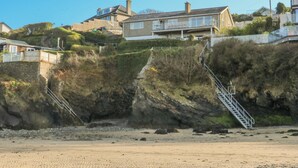Une zone résidentielle côtière avec des maisons, une plage de sable et un escalier menant au sommet d’une falaise.