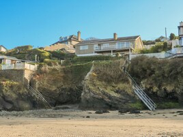 Zona residencial costera con casas, una playa de arena y una escalera que sube por un acantilado.