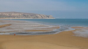 Une plage avec un rivage sablonneux, une mer calme et une falaise qui se dessine à l’horizon.