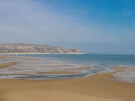 Una playa con arena, mar tranquilo y un acantilado lejano.