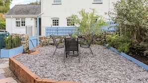 A patio with a table and chairs, surrounded by a stone wall and a blue fence. - Bryn Bach (Pentraeth)