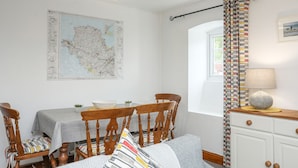 A dining area with a map on the wall, a table with chairs, a window with curtains, and a lamp on a cabinet. - Bryn Bach (Pentraeth)