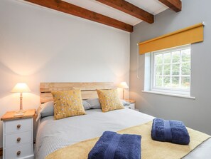 A bedroom with a bed, two bedside lamps, a window with a yellow blind, and a wooden headboard. - Bryn Bach (Pentraeth)