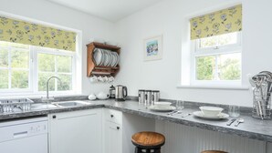 A modern kitchen with white cabinets, a granite countertop, and two wooden stools. - Bryn Bach (Pentraeth)