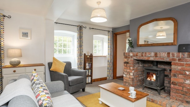 A cozy living room with a fireplace, a sofa, a coffee table, and a bookshelf. - Bryn Bach (Pentraeth)