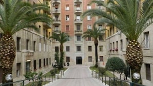 A multi-story building with a central courtyard, surrounded by palm trees and a pedestrian pathway.