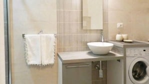 A modern bathroom with a large mirror, a sink, a towel rack, and a washing machine.