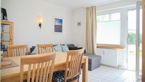 Ein Essbereich mit einem Holztisch und -stühlen, einem grauen Sofa und Blick ins Freie durch ein großes Fenster.