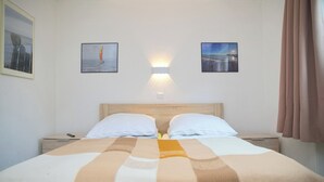 Ein Hotelzimmer mit einem Bett, zwei Kissen, einem Nachttisch, einer Wandleuchte und zwei gerahmten Bildern.