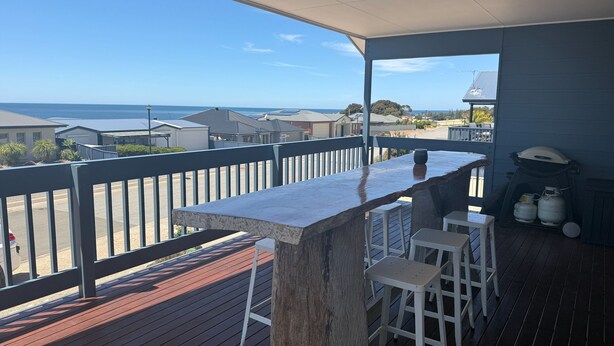 A covered outdoor area with a wooden deck, a bar counter, and white bar stools. - Seaviews at Stansbury - Modern and spacious! Off Peak special available! (Stansbury)
