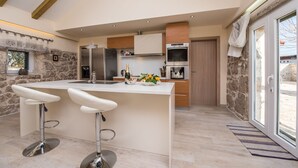 A modern kitchen with a central island, bar stools, a stone wall, and a large window. - Villa Didova kuća ZadarVillas (Podlug)