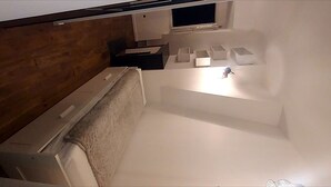 Une pièce avec un plancher en bois, un lit blanc et un luminaire au plafond.