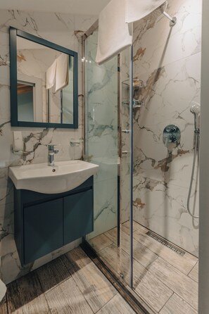 A bathroom with a marble wall, a sink with a mirror, and a glass shower enclosure. - Capital City Hotel (Baku)