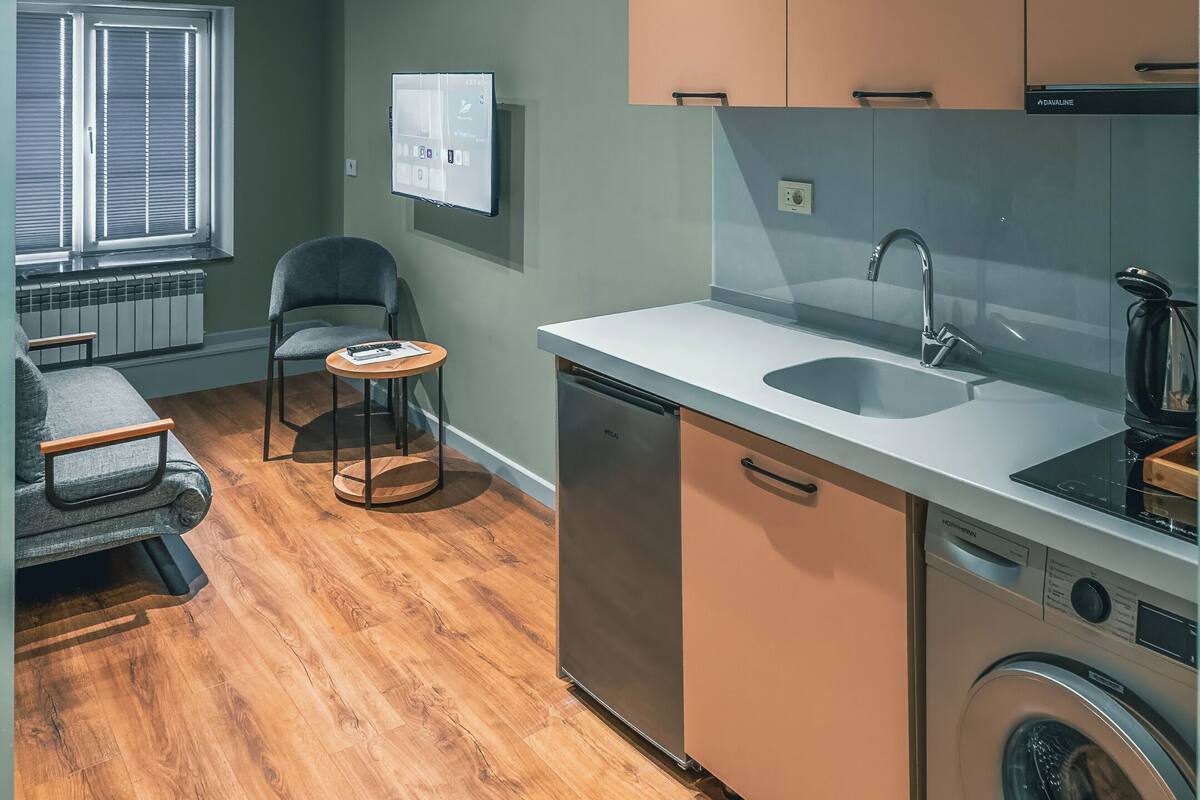 Una cocina compacta con lavadora integrada, un pequeño comedor y un ventanal con persianas.