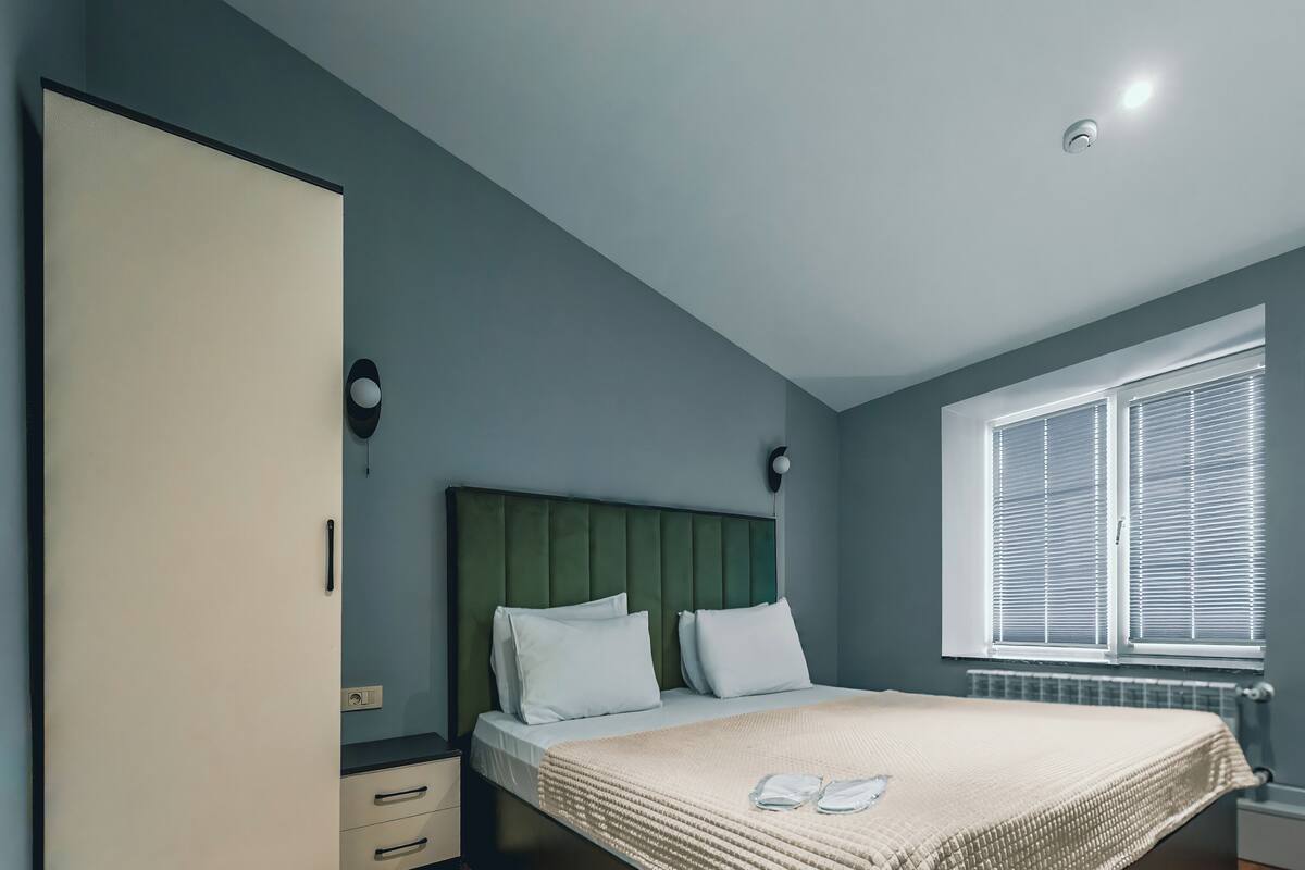 Un dormitorio con cama, armario, mesita de noche y ventana con persianas.