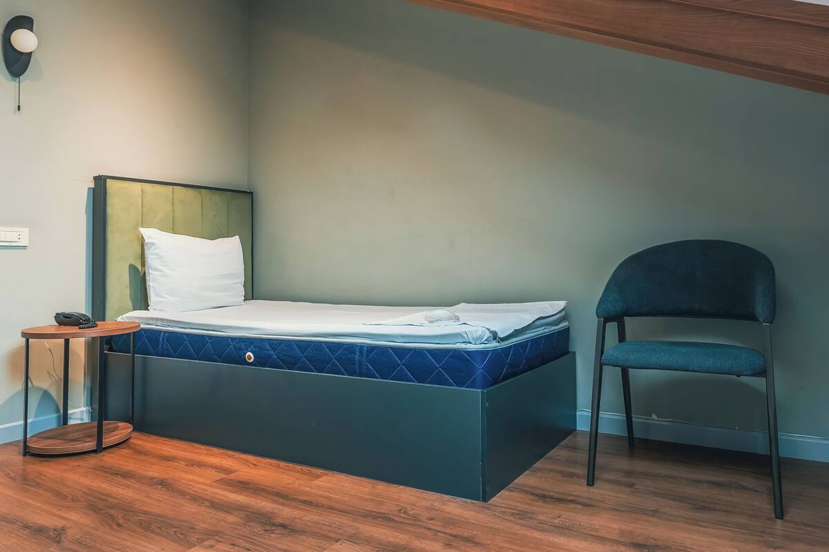 Un dormitorio con tragaluz, una cama, una silla y suelo de madera.
