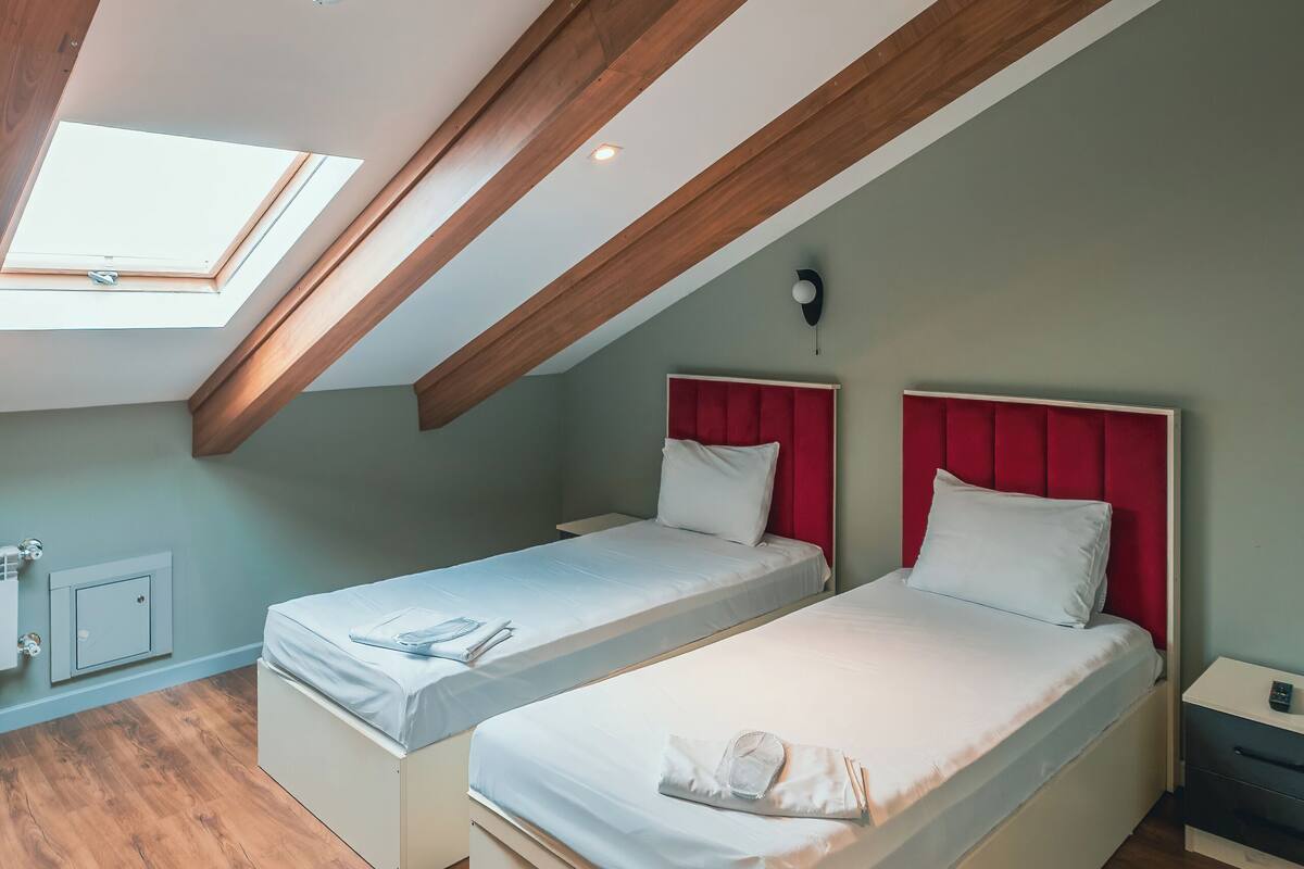 Habitación con dos camas, vigas de madera, tragaluz y una mesita de noche.