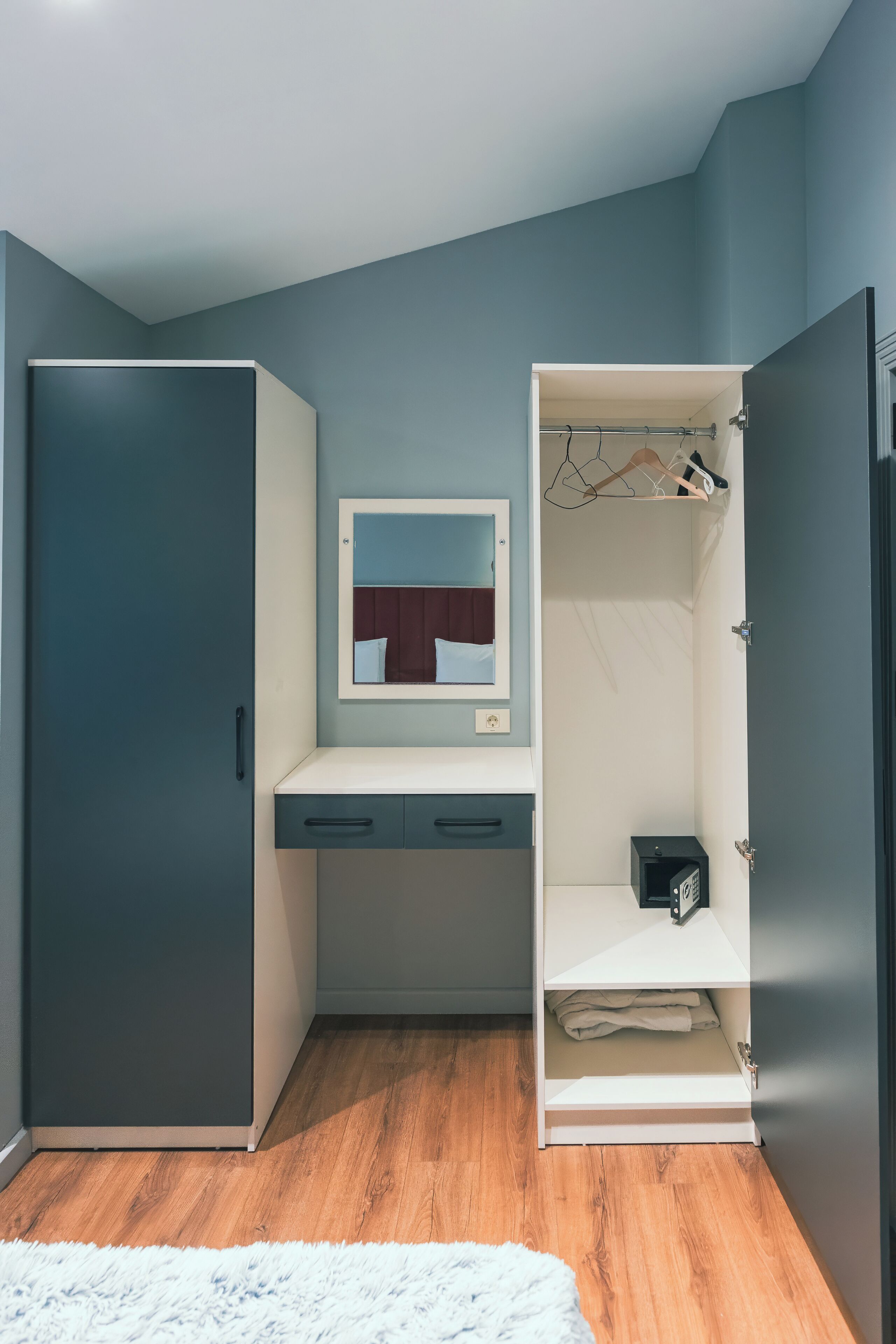 A bedroom with a wardrobe, a bedside table, a mirror, and a hanging clothes rack.