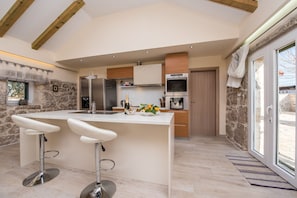 A modern kitchen with a central island, bar stools, a stone wall, and a large window. - Villa Didova Kuća Zadarvillas (Benkovac)