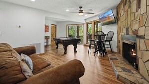 A living room with a pool table, a fireplace, a ceiling fan, and a TV mounted on the wall. - 5BR Gatlinburg Family Getaway with Views, Hot Tub & Game Room in Chalet Village (Gatlinburg)