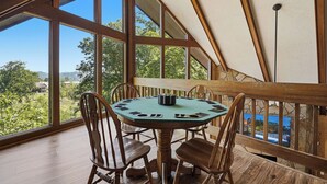 A round wooden table with chairs, large windows, and a view of greenery and hills. - 5BR Gatlinburg Family Getaway with Views, Hot Tub & Game Room in Chalet Village (Gatlinburg)