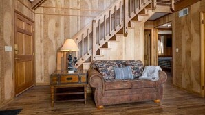 A wooden-floored room with a staircase, a brown leather sofa, and a lamp. - 5BR Gatlinburg Family Getaway with Views, Hot Tub & Game Room in Chalet Village (Gatlinburg)