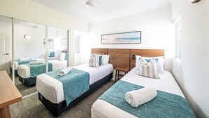 Habitación de hotel con dos camas, un espejo grande y vista al mar.