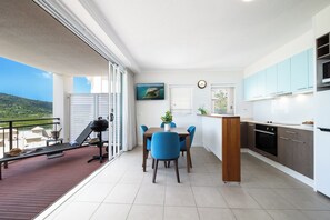 A modern kitchen with a dining area, a balcony with a grill, and a view of the landscape. - Port Views On Airlie Premier (Airlie Beach)