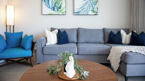 Una sala de estar moderna con un sofá gris, cojines azules, un adorno blanco y dos cuadros enmarcados con hojas en la pared.