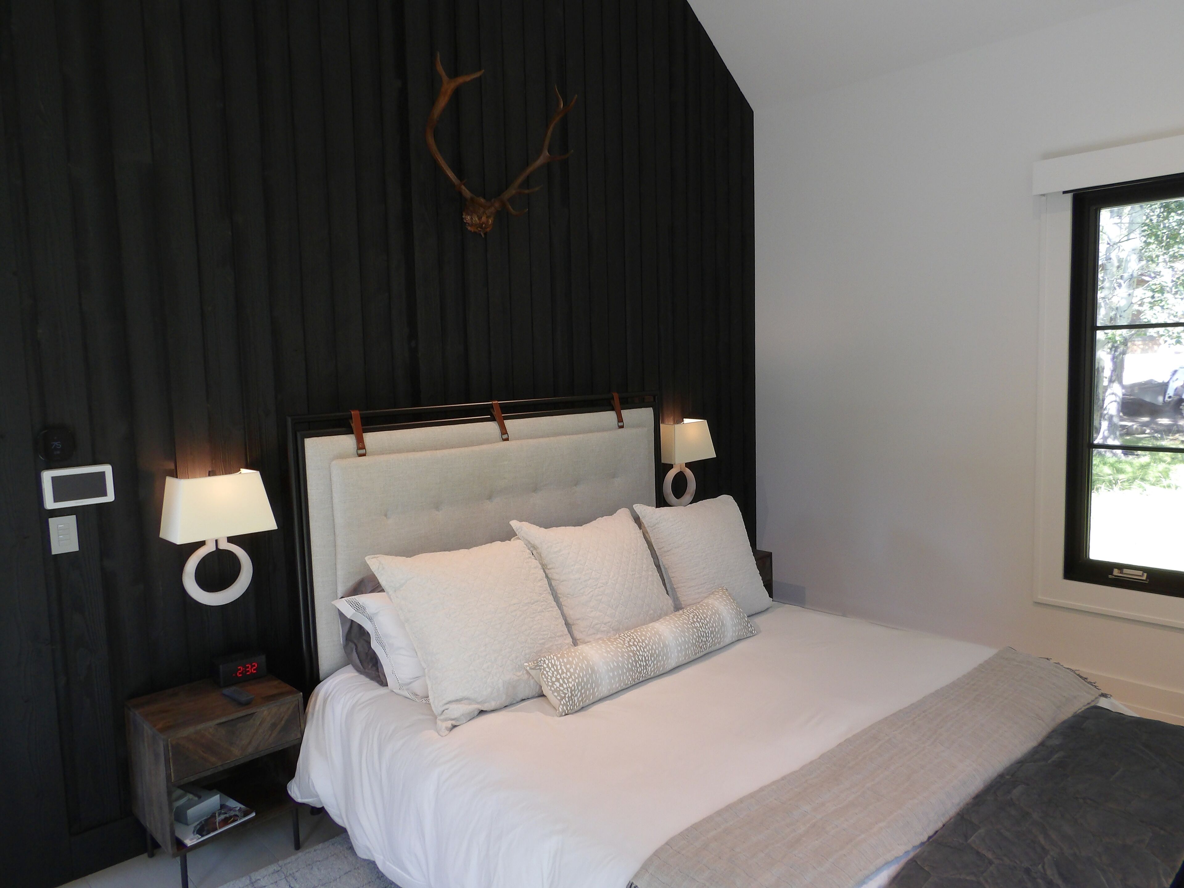 Une chambre à coucher avec un grand lit, deux lampes de chevet, une horloge murale et une fenêtre donnant sur des arbres.
