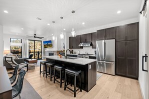 A modern kitchen with dark cabinets, stainless steel appliances, and a central island with bar stools. - Rooftop Haven | Hot Tub, BBQ & Views of Buffalo Mountain (Silverthorne)