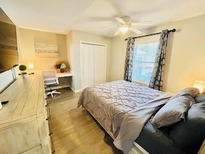 A bedroom with a bed, a desk, a chair, a ceiling fan, and a window with curtains.