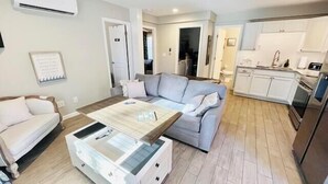 Un salon moderne comprenant un canapé, une table basse et un coin cuisine avec des placards et des appareils électroménagers.