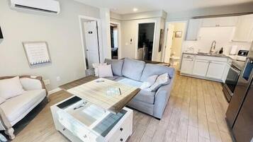 Un salon moderne comprenant un canapé, une table basse et un coin cuisine avec des placards et des appareils électroménagers.