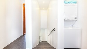A modern staircase with a handrail, leading to a laundry area with a white washing machine and a blue towel on top. - Gabriella Villa ONE -Grace Bay, Hot Tub, Pool, Events allowed - NEW VILLA (Providenciales)