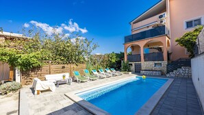 A swimming pool with lounge chairs, a stone wall, and a building with balconies. - Charming three-bedroom apartment near the sea (Valbandon)