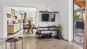 A modern kitchen with wooden cabinets, a dining area with a table and chairs, a TV mounted on the wall, and a sliding glass door leading to an outdoor area. - Charming three-bedroom apartment near the sea (Valbandon)