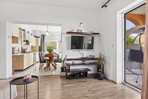 A modern kitchen with wooden cabinets, a dining area with a table and chairs, a TV mounted on the wall, and a sliding glass door leading to an outdoor area. - Charming three-bedroom apartment near the sea (Valbandon)