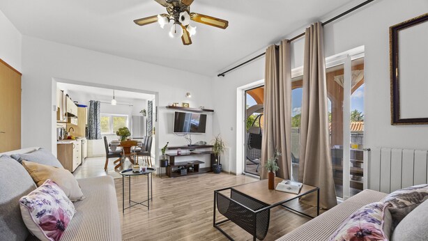 A modern living room with a sofa, coffee table, and TV. There is a kitchen in the background with a dining area. - Charming three-bedroom apartment near the sea (Valbandon)